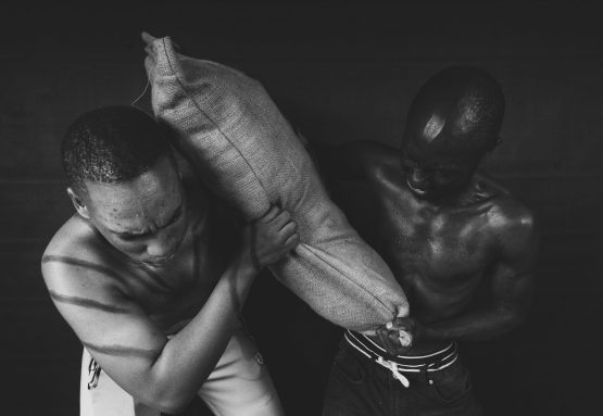 Two farm workers helping each other to pick up a sack of potatoes.One of them is bruised from the sjambok beatings to show the unfair treatment the farmers got while working.